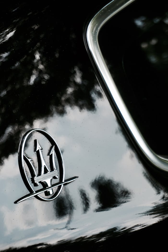 Detailed close-up of Maserati logo reflecting on a shiny black car surface, showcasing luxury branding.